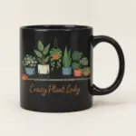 Black ceramic mug with illustrated potted plants and Crazy Plant Lady printed on the front.